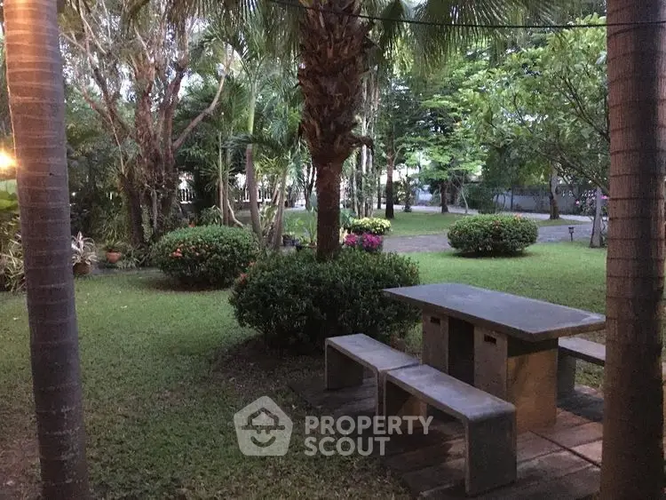Charming garden area with concrete picnic table surrounded by lush greenery and trees.