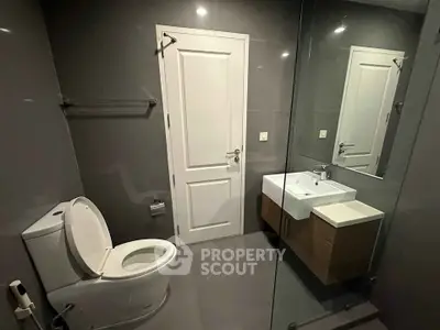 Modern bathroom with sleek design, featuring a glass shower, white sink, and toilet in a contemporary setting.