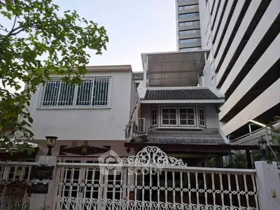 Charming two-story house with decorative wrought iron gate and modern high-rise backdrop.