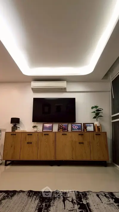 Modern living room with sleek wooden cabinet, wall-mounted TV, and ambient ceiling lighting.