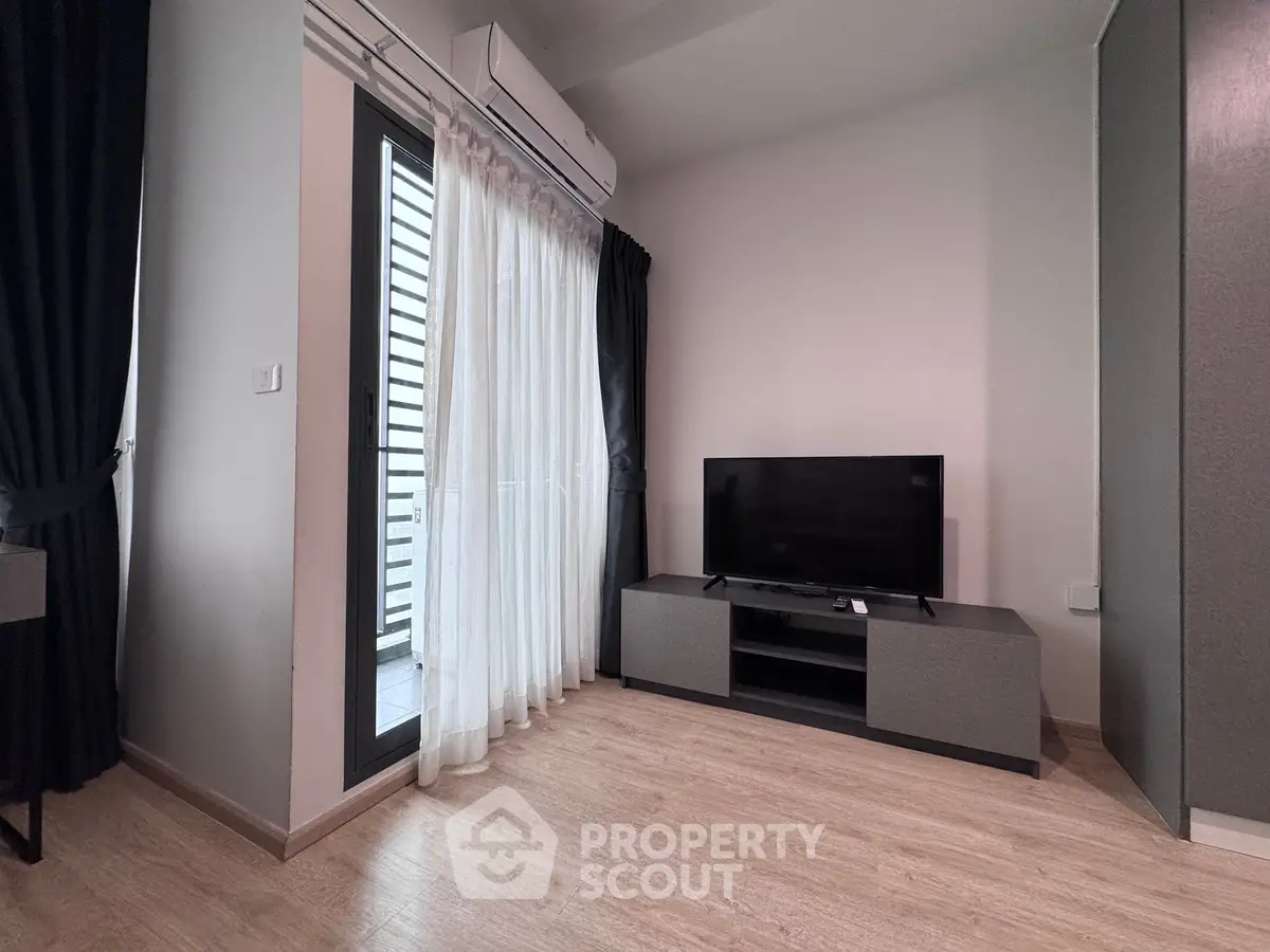 Modern living room with sleek TV setup and balcony access, featuring elegant curtains and wood flooring.
