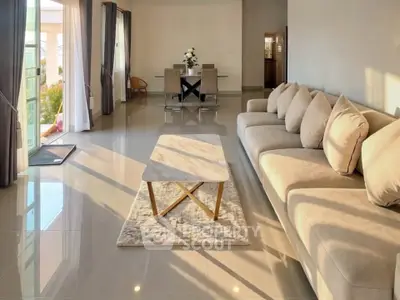 Spacious living room with elegant sofa and dining area, featuring large windows and abundant natural light.
