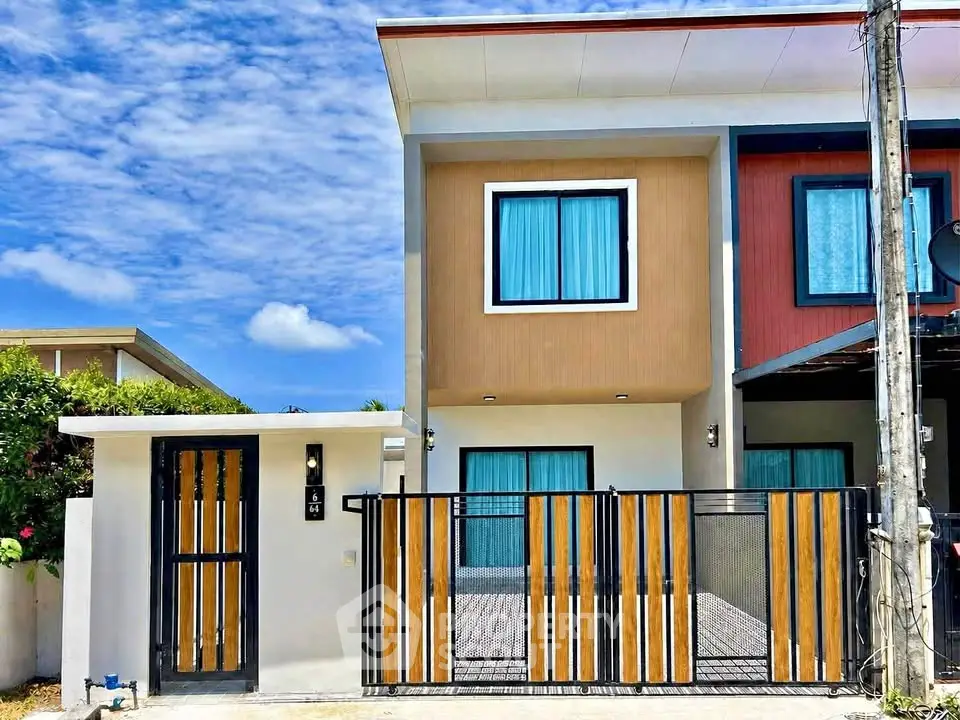 Modern two-story townhouse with vibrant facade and gated entrance under a clear blue sky.
