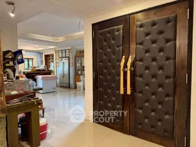 Spacious living area with unique padded double doors and modern kitchen in the background.