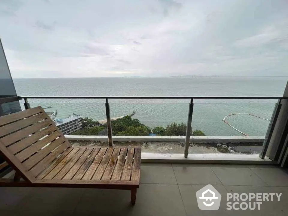 Stunning ocean view from modern balcony with wooden lounger, perfect for relaxation and enjoying sunsets.