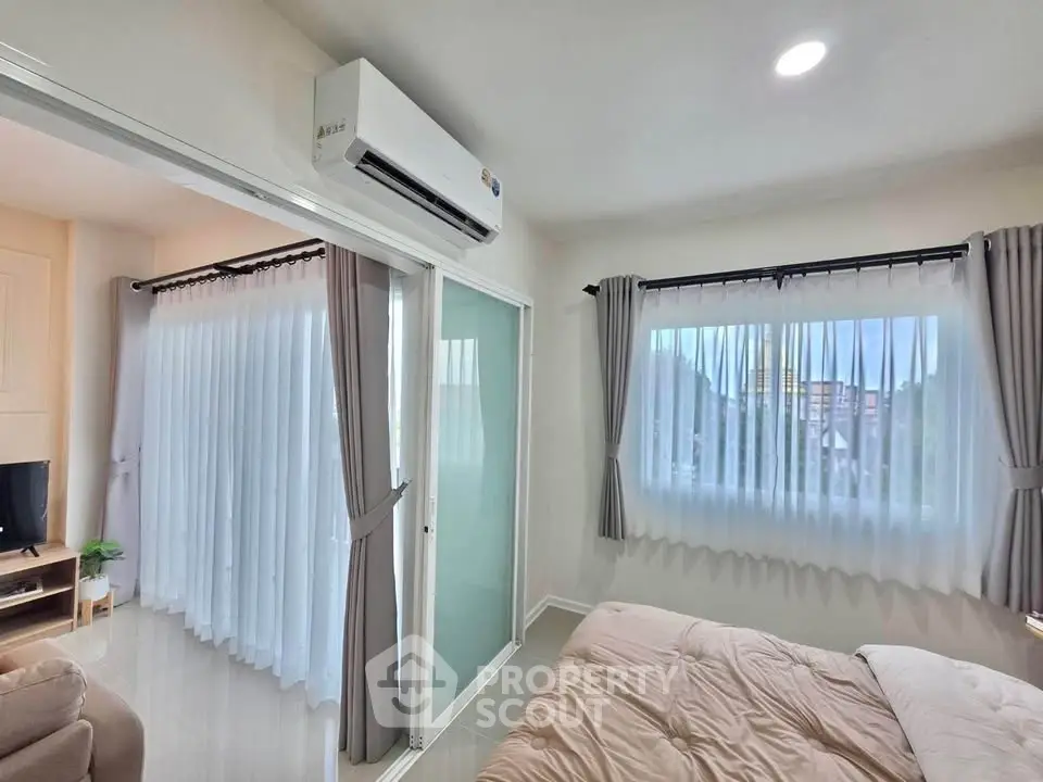 Modern bedroom with large windows and air conditioning, featuring a cozy bed and sliding glass doors.