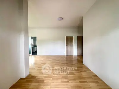 Spacious empty room with wooden flooring and two doors, ideal for customization.