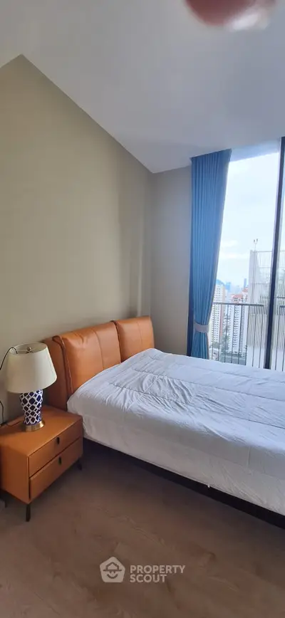 Modern bedroom with city view, featuring stylish orange bed and elegant blue curtains.
