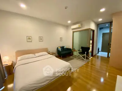 Spacious modern bedroom with wooden flooring and cozy seating area