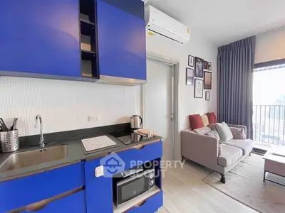 Modern apartment interior with vibrant blue kitchen and cozy living area, featuring a balcony view.