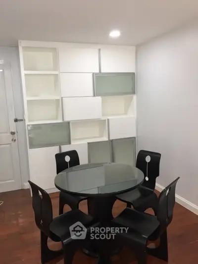 Modern dining area with sleek black chairs and glass table, featuring stylish built-in shelving.