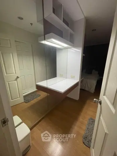 Modern bedroom with sleek built-in vanity and mirror, featuring wooden flooring and ambient lighting.