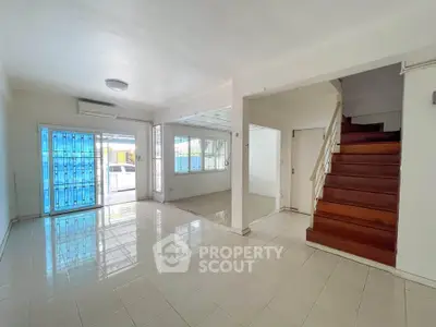 Spacious living room with tiled floors and wooden staircase in a bright, airy home.
