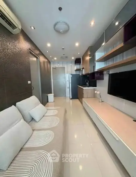 Modern living room with sleek design, featuring a comfortable sofa, wall-mounted TV, and stylish kitchen area.
