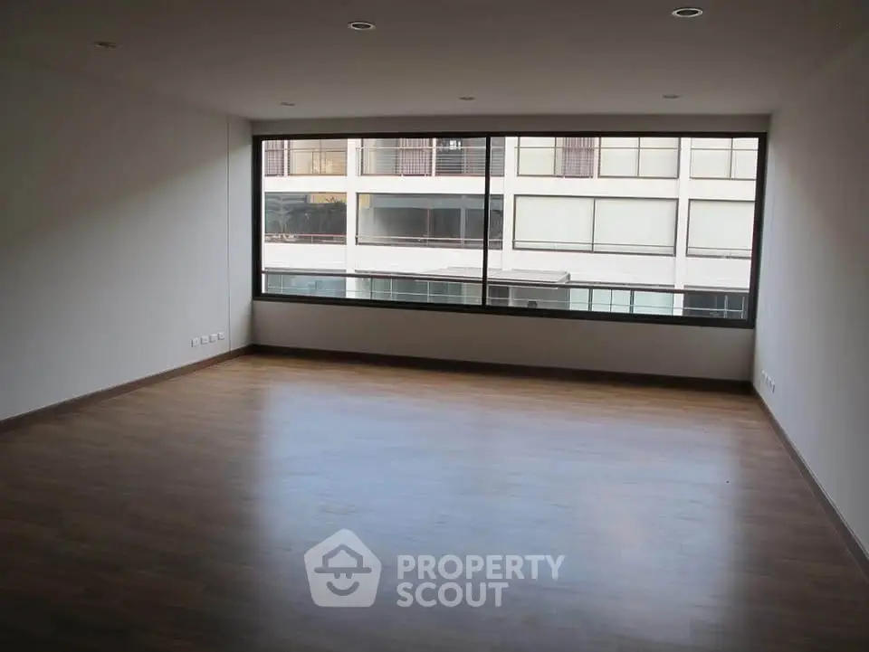 Spacious empty room with large window and wooden flooring in modern apartment.
