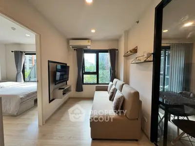 Modern living room with cozy sofa and wall-mounted TV, adjacent to a bright bedroom with large windows.