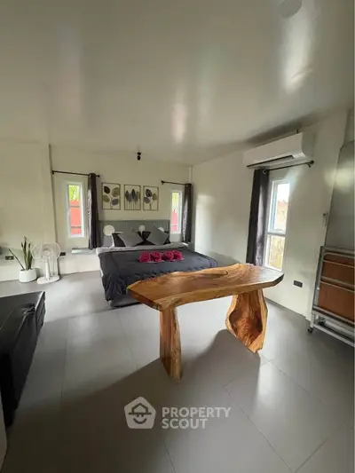 Spacious bedroom with modern decor and unique wooden table, featuring natural light and stylish furnishings.