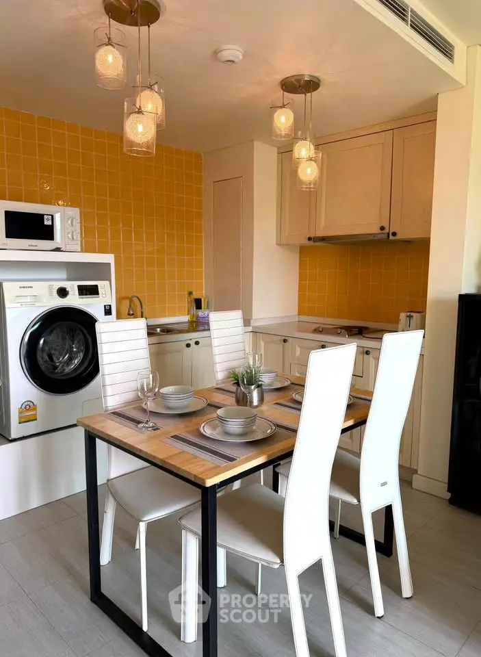 Modern kitchen with dining area, featuring washing machine and stylish lighting.