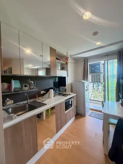 Modern kitchen with sleek cabinetry and natural light, featuring a compact dining area and balcony access.