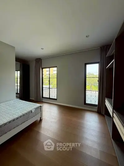 Spacious bedroom with large windows and wooden flooring, offering ample natural light and modern design.