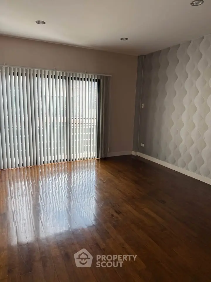 Spacious empty living room with wooden floors and large window blinds.