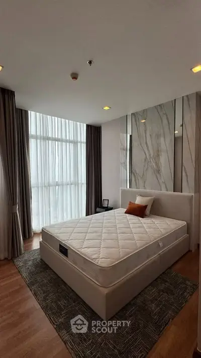 Spacious bedroom with large windows and elegant decor in modern apartment.