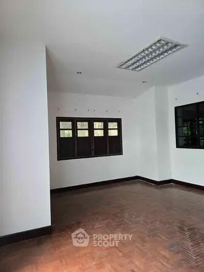 Spacious room with wooden flooring and large windows, ideal for versatile interior design.