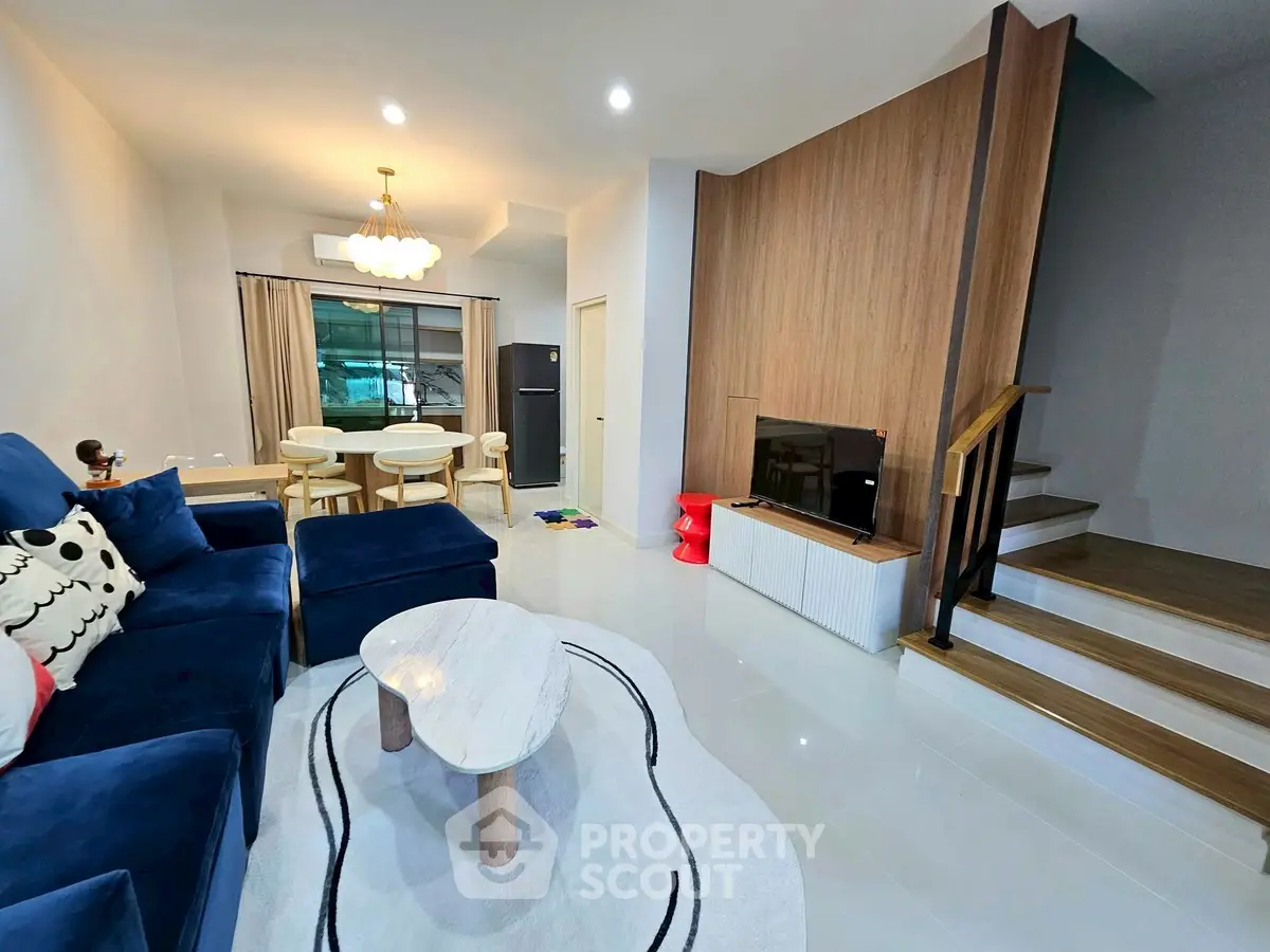 Modern living room with stylish furniture and open dining area, featuring elegant lighting and cozy ambiance.