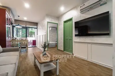 Modern living room with wooden flooring, large TV, and dining area in open layout.