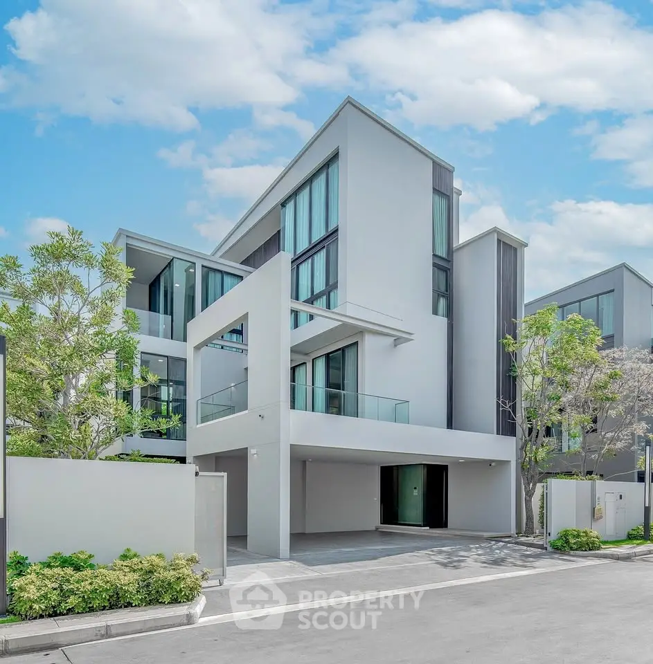 Modern luxury three-story house with sleek design and large windows under a clear blue sky.