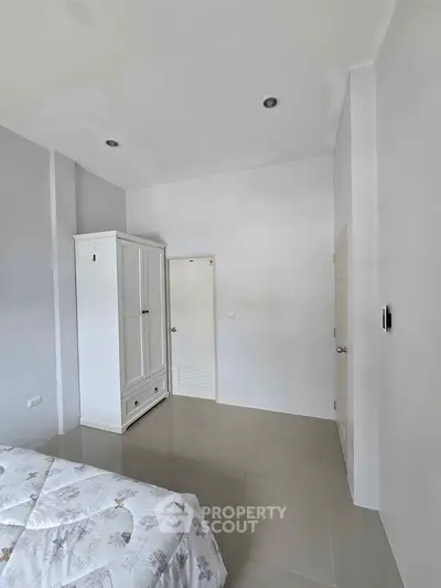 Minimalist bedroom with white wardrobe and bed, featuring sleek tiled flooring.