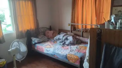 Cozy bedroom with natural light and wooden flooring, featuring a comfortable bed and a fan for ventilation.