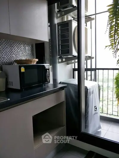 Modern kitchen with microwave and balcony view, featuring sleek cabinetry and natural light.