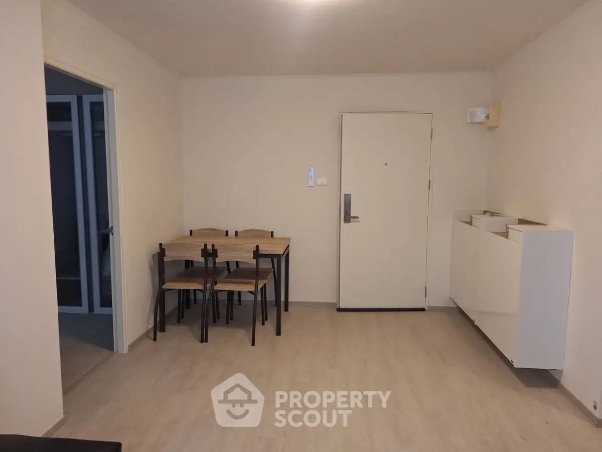 Minimalist dining area in modern apartment with wooden table and chairs, light flooring, and white walls.