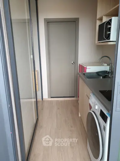 Compact modern kitchen with washing machine and microwave, featuring sleek cabinetry and wood flooring.