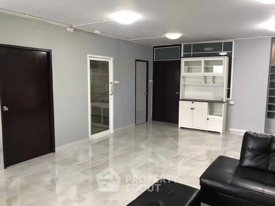 Spacious modern living room with sleek black leather furniture and elegant white cabinetry.