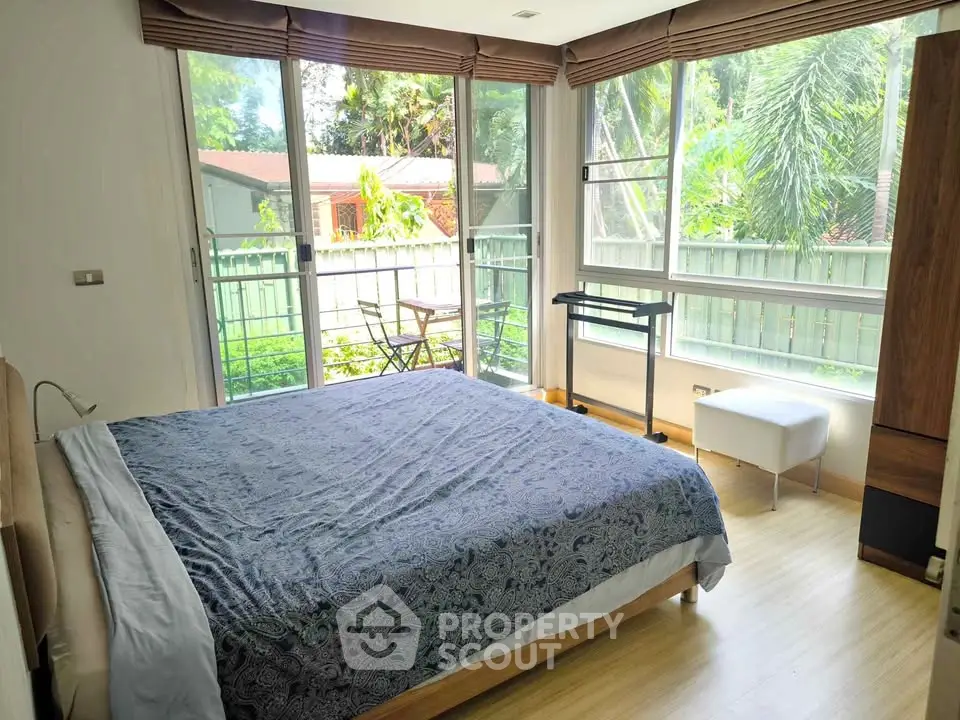 Bright bedroom with large windows and garden view, featuring a cozy bed and modern decor.