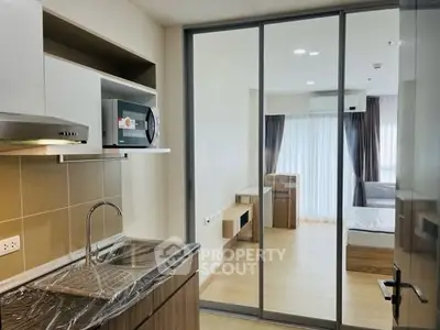 Modern apartment with sleek kitchen and cozy bedroom separated by glass sliding doors.