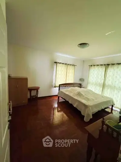Spacious bedroom with wooden flooring and natural light