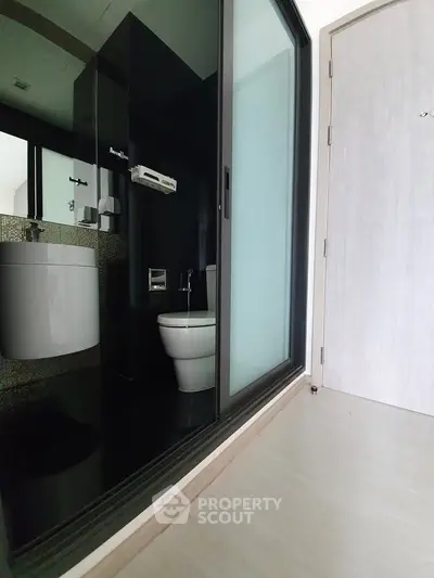 Modern bathroom with sleek black tiles and glass sliding door in contemporary apartment.
