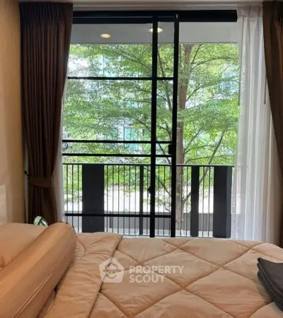 Cozy bedroom with a view of lush greenery from a large window, perfect for relaxation.