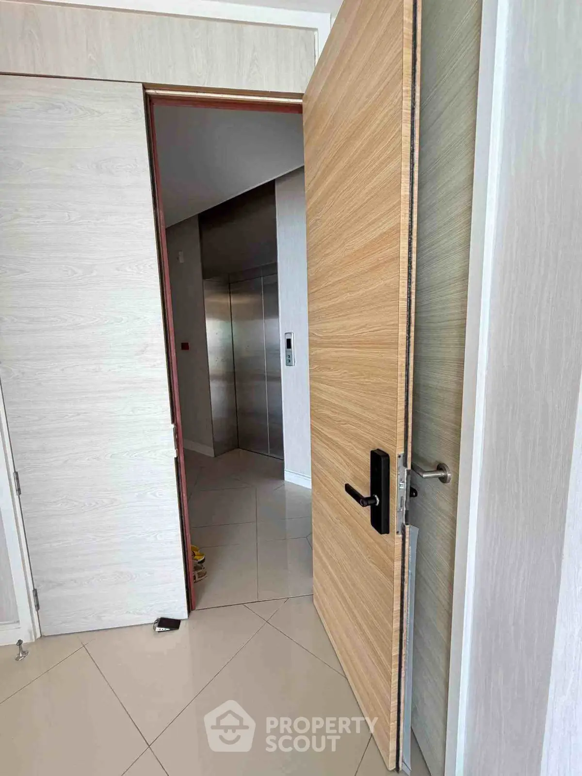 Modern apartment entrance with view of elevator, showcasing sleek wooden door and tiled flooring.