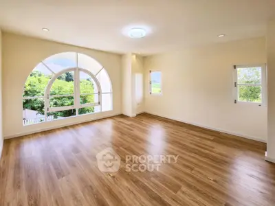 Spacious empty room with large arched window and wooden flooring