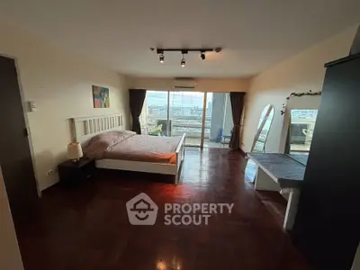 Spacious bedroom with balcony and city view, featuring wooden flooring and modern decor.