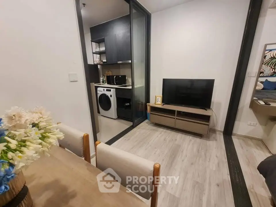 Modern apartment interior with open living room and kitchen featuring washing machine and TV setup.