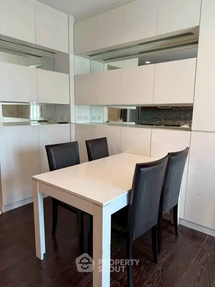 Modern dining area with sleek white table and dark chairs, featuring stylish cabinetry and hardwood floors.