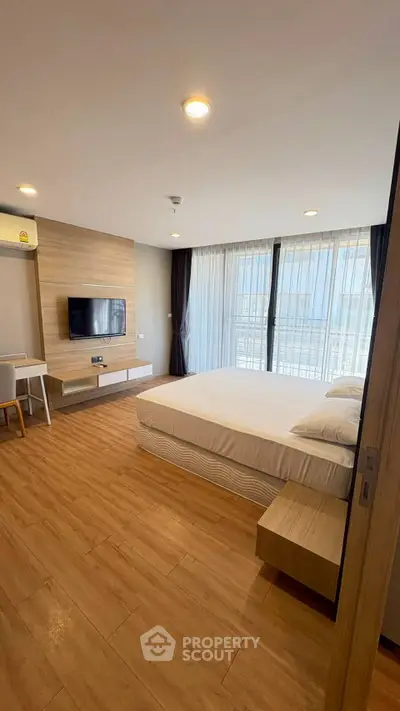 Modern bedroom with wooden flooring and large windows for natural light.