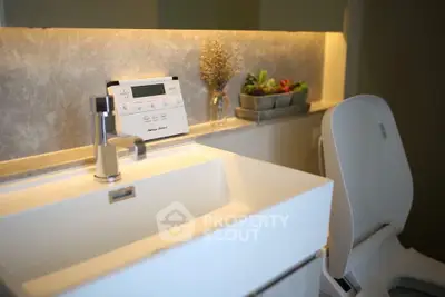 Modern bathroom with sleek sink and toilet, featuring ambient lighting and decorative plants.