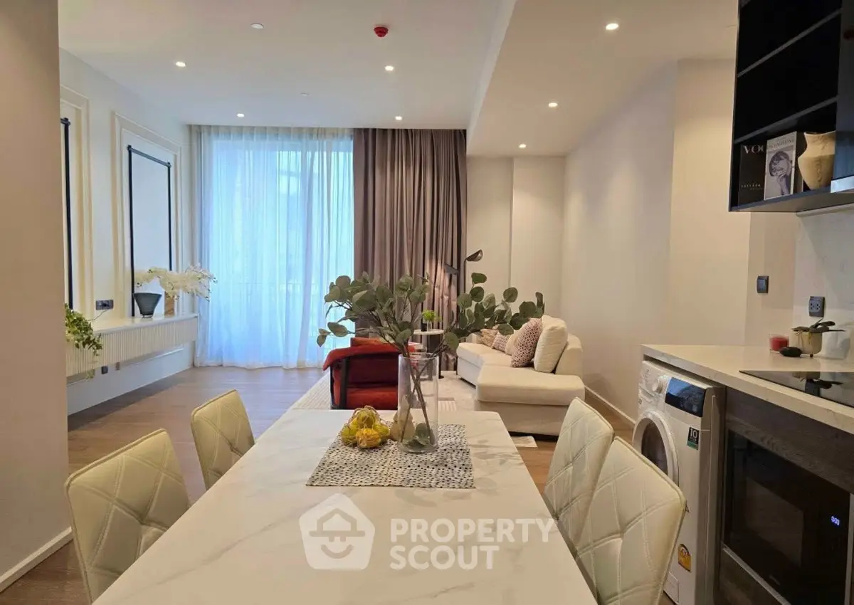 Modern open-plan living room with dining area and washing machine, featuring elegant decor and natural light.