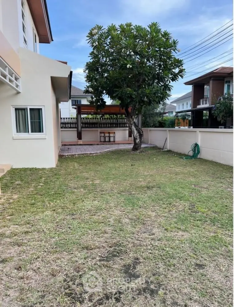 Spacious backyard with lush lawn and mature tree in suburban home setting.